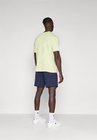 Light yellow t-shirt, short sleeves, loose fit; paired with navy shorts. Complete look includes white sneakers and white socks.
