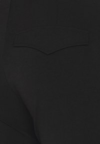 Jeans de denim preto com um bolso traseiro curvado e detalhes de costura subtil. O tecido tem uma textura suave, destacando um design ajustado.