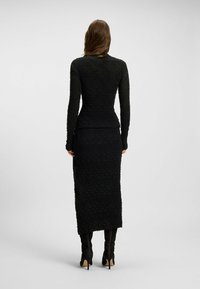 Schwarzes Strickkleid mit langen Ärmeln, das ein strukturiertes Blumenmuster und eine figurnahe Silhouette aufweist, die bis zur Mitte der Wade reicht.