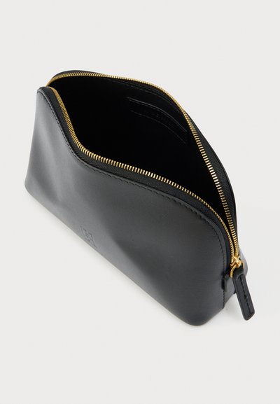 Μαύρο δερμάτινο τσαντάκι με λεία υφή, χρυσλό φερμουάρ και στρογγυλεμένη κορυφή. Ανοιχτό υπό γωνία, δείχνοντας κενό εσωτερικό. Χωρίς εμφανές λογότυπο.