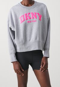 Grå sweatshirt med rund halsringning, droppade axlar och cropped design. Har rosa DKNY New York-tryck över bröstet.