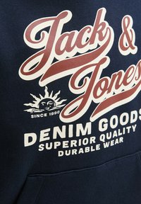 Hoodie bleu marine avec texte blanc et bordeaux, logo "Jack & Jones", graphique de soleil et étiquette "Denim Goods". Matière en mélange de coton.