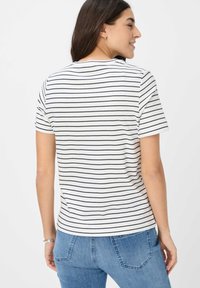 Witte t-shirt met korte mouwen en marineblauwe horizontale strepen; ronde halslijn; ontspannen pasvorm; zachte katoenstof; gecombineerd met blauwe jeans.