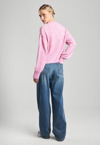 Pink fuzzy sweater with a loose fit and ribbed hem, paired with light blue wide-leg jeans featuring back pockets and a faded texture.