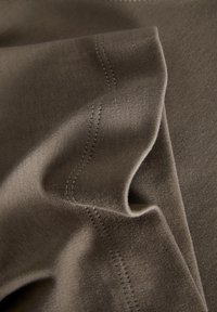 Olivově zelená tkanina s hladkým povrchem, složená tak, aby byly vidět detaily stehu a jemné úpravy odstínu.