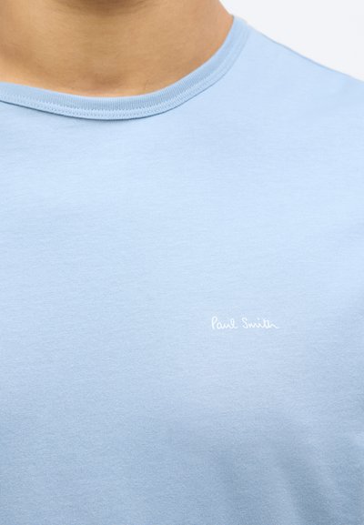 Tricou din bumbac de culoare albastru deschis, cu guler rotund și mâneci scurte. Are logo-ul brodat "Paul Smith" în alb. Textură netedă.