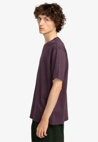 Camiseta de algodón morada con mangas cortas, cuello redondo y detalles de costura mínimos, mostrada llevada por una persona.