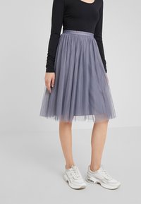 Gonna in tulle grigia con un motivo a pois, vita arricciata, abbinata a sneakers bianche. La gonna ha una texture a strati e leggera.