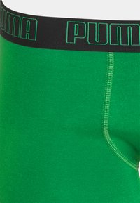 Grüne Boxer-Briefs mit einem schwarzen Bund, der das Logo "PUMA" in grünen Buchstaben zeigt. Glattes Material mit flachen Nähten.