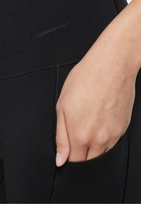 Czarne legginsy sportowe z boczną kieszenią. Wykonane z gładkiego, elastycznego materiału z subtelnym czarnym logo Nike. Zawierają ozdobne szwy.
