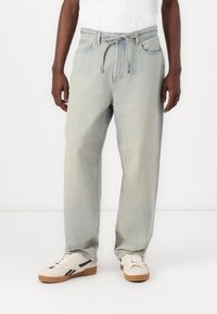 Lyseblå denimjeans med afslappet pasform, snøring i taljen og fem lommer, parret med cremefarvede sneakers med sorte accenter.