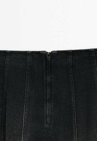 Gros plan de la partie supérieure d'une jupe en jean noire avec une fermeture éclair centrale fermée et des lignes de couture verticales visibles.