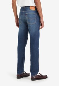 Jean en denim bleu à jambe droite avec une finition délavée, patch en cuir à la taille et poches arrière standards. Design classique à cinq poches.