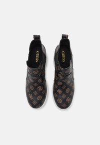 Scarpe nere slip-on con un design a motivo marrone che presenta dei loghi. Materiale in pelle liscia con una suola in gomma bianca.