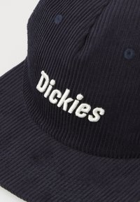 Gorra de terciopelo de color azul marino oscuro con el logotipo bordado de "Dickies" en blanco. Tela texturizada con costillas visibles y detalles de costura contrastantes.
