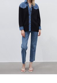 Svart stickad tröja med denimkrage, knappar framtill och två bröstfickor. Kombinerad med ljusblå raka jeans och vita sandaler.