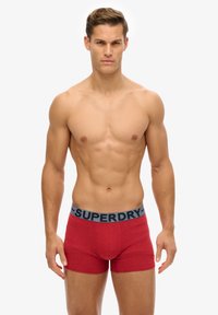 Czerwone bawełniane slipy typu boxer z szarym pasem w logo "SUPERDRY". Design jest dopasowany, o gładkiej fakturze i bez widocznych wzorów.