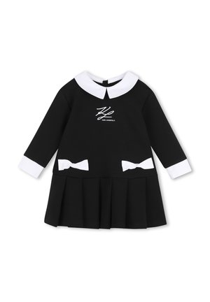 Robe noire à manches longues avec col Claudine blanc, poignets blancs, deux nœuds blancs à la taille et jupe plissée, avec logo Karl Lagerfeld.