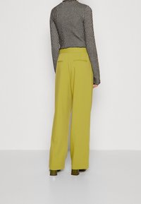 Pantaloni a gamba larga in un tessuto giallo brillante con una texture liscia, abbinati a una maglia a maniche lunghe a righe bianche e nere.