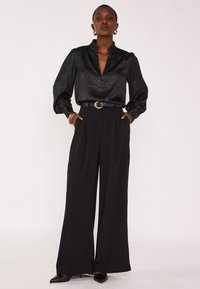 Black blouse with a ruffled neckline and long sleeves, paired with high-waisted, wide-leg black trousers and pointed black heels.