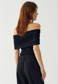 Čierny top bez ramienok so zbrúsenou textúrou, priliehajúci strih a krátke rukávy, skombinovaný s míňanými čiernymi nohavicami.