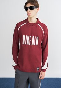 Sweatshirt bege com detalhes brancos, apresentando um grande logo "NIKE AIR". Manga longa e um corte descontraído, feito de material suave.
