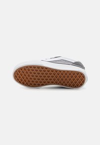 Baskets blanches avec des accents gris, dotées d'une semelle en caoutchouc texturé avec un motif en nid d'abeille et un dessous brun contrastant.