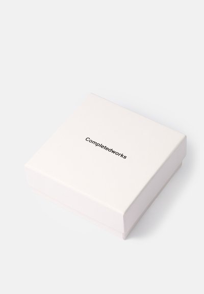 Bijela kutija za nakit u obliku kvadrata s crnim logotipom "Completedworks" centriranim na poklopcu, postavljena na bijeloj pozadini.