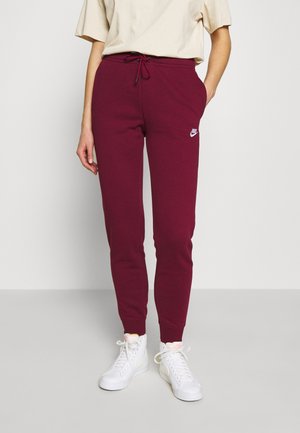 Personne portant un pantalon de survêtement Nike bordeaux avec taille à cordon et des baskets montantes blanches, debout devant un fond uni.