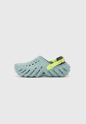 Sabot bleu clair à enfiler avec des trous de ventilation, semelle épaisse rainurée et bride de talon ajustable vert néon sur fond uni.