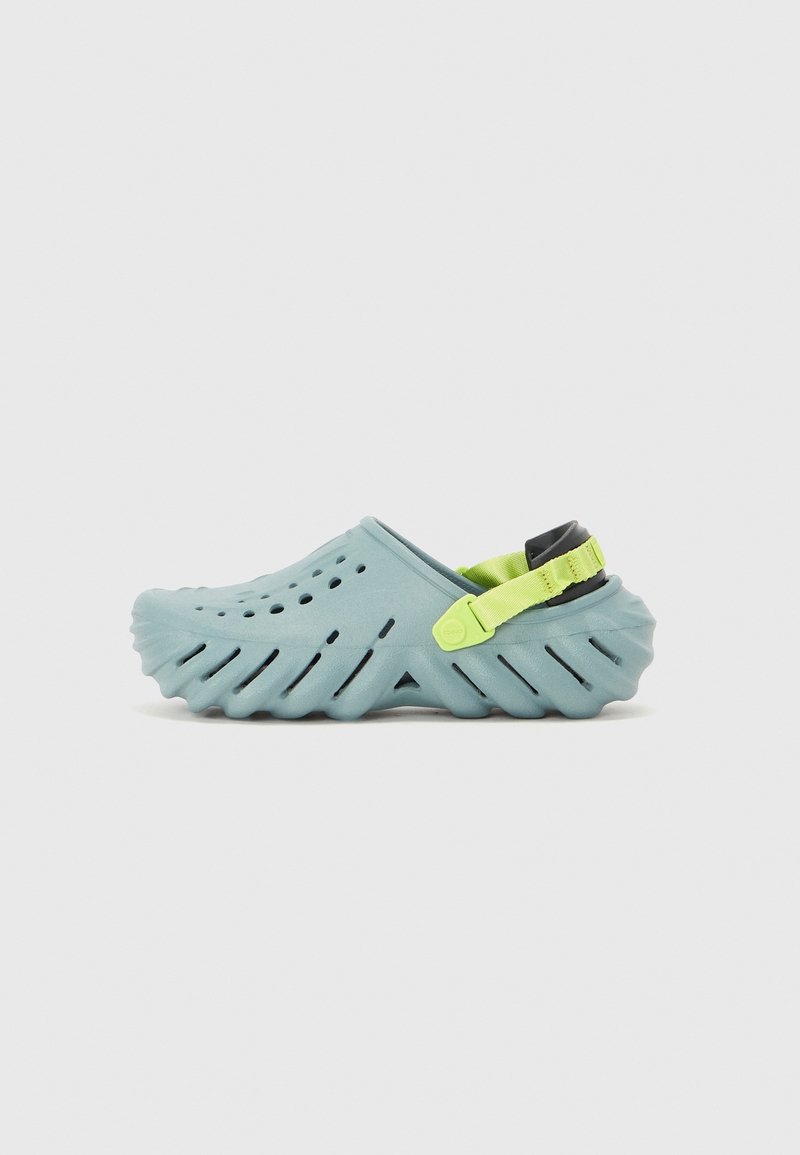 Sabot bleu clair à enfiler avec des trous de ventilation, semelle épaisse rainurée et bride de talon ajustable vert néon sur fond uni.