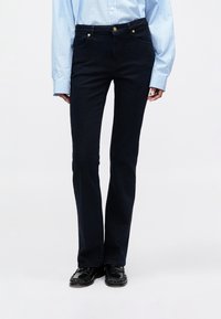 Mørkeblå flared jeans med en glat tekstur, høj talje, fire lommer, guldknapdetaljer, parret med en lyseblå stribet skjorte.