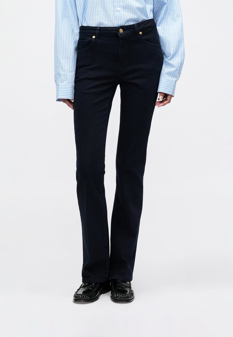 Mørkeblå flared jeans med en glat tekstur, høj talje, fire lommer, guldknapdetaljer, parret med en lyseblå stribet skjorte.