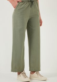Hellgrüne, weit geschnittene Hosen mit elastischem Bund und Kordelzug. Sie sind mit seitlichen Taschen und fransigen Saumdetails ausgestattet und werden mit beigen Sneakern kombiniert.