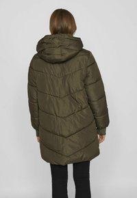 Mīksts tumši olīvzaļš mētelis ar kapuci, ar ševronu izšuvumu, garām piedurknēm un brīvā piegriezuma, sasniedz vidus celi.