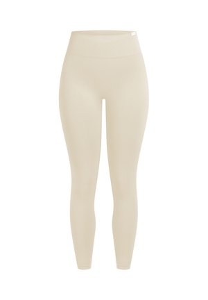 Leggings beiges taille haute sans coutures avec une large ceinture élastique et une coupe longueur cheville sur fond blanc.