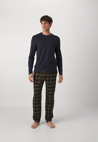 Vīriešu naktsģērbu komplekts ar tumši zilu krekliņu ar garām piedurknēm un zaļā krāsā rūtainām biksēm. Audums izskatās mīksts, ar vaļēju piegriezumu un elastīgu jostasvietu.