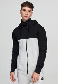 Felpa zip con cappuccio nera e grigia con colletto alto, caratterizzata da una texture liscia, cappuccio con cordino e tasche laterali.