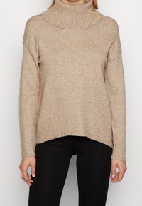 Beżowy sweter na wysoki kołnierz o luźnym kroju, z prążkowanym dekoltem i dołem. Wykonany z miękkiego materiału o lekko teksturowanym wykończeniu.