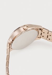 Reloj de metal en oro rosa con una caja circular y suave y una pulsera de eslabones. Incluye una corona texturizada y una esfera minimalista sin marcas.