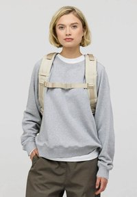Grå crewneck sweatshirt med ribbade ärmar och kant, bärs över en vit skjorta. Beige ryggsäcksremmar med ett spänne över bröstet.