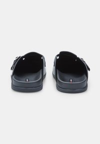Fekete slip-on szandál sima szintetikus felsőrésszel, nyitott hátsó résszel és állítható pánttal. Kényelmes talpbetéttel és lapos talppal rendelkezik.