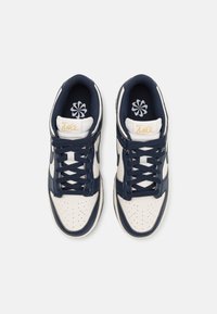 Navy and cream Nike sneakers with a lace-up design, perforated toe, padded collar, gold logo, and blue floral pattern on the insole.