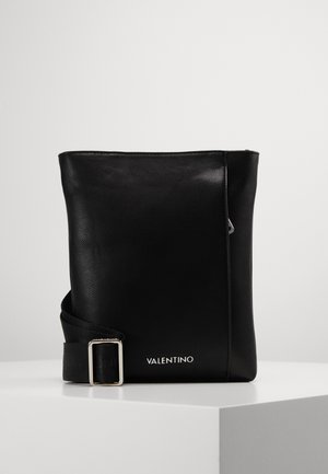 Czarna torba typu crossbody Valentino z regulowanym paskiem, srebrną sprzączką i logo na gładkiej skórzanej powierzchni na białym cokole.