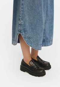 Jeans krilo z razširjenim robom, ki ima asimetričen kroj. V kombinaciji s črnimi usnjenimi mokasini na debelih platformah.