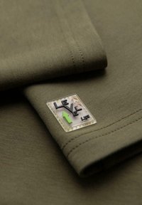 Oliven grøn t-shirt i bomuld med et struktureret mærke med "LEVEL UP" i sort, orange og grøn, placeret på ærmet.