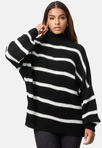 Maglione a collo alto a righe bianche e nere, con una vestibilità ampia, polsini e orlo a costine. Il filato testurizzato aggiunge dimensione.