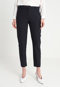 Navy trousers in a fitted design with a smooth texture, featuring a classic waistband and tapered legs, paired with white heels.