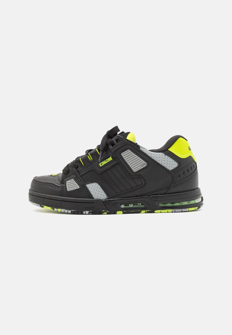 Black sneaker with yellow accents and grey mesh panels. Features a rounded toe, textured overlays, and a visible air cushion in the sole.