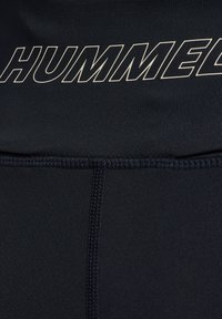 Sort stof med synlige syninger og fed, hvidt omridset "HUMMEL" tekst trykt hen over den øverste del.